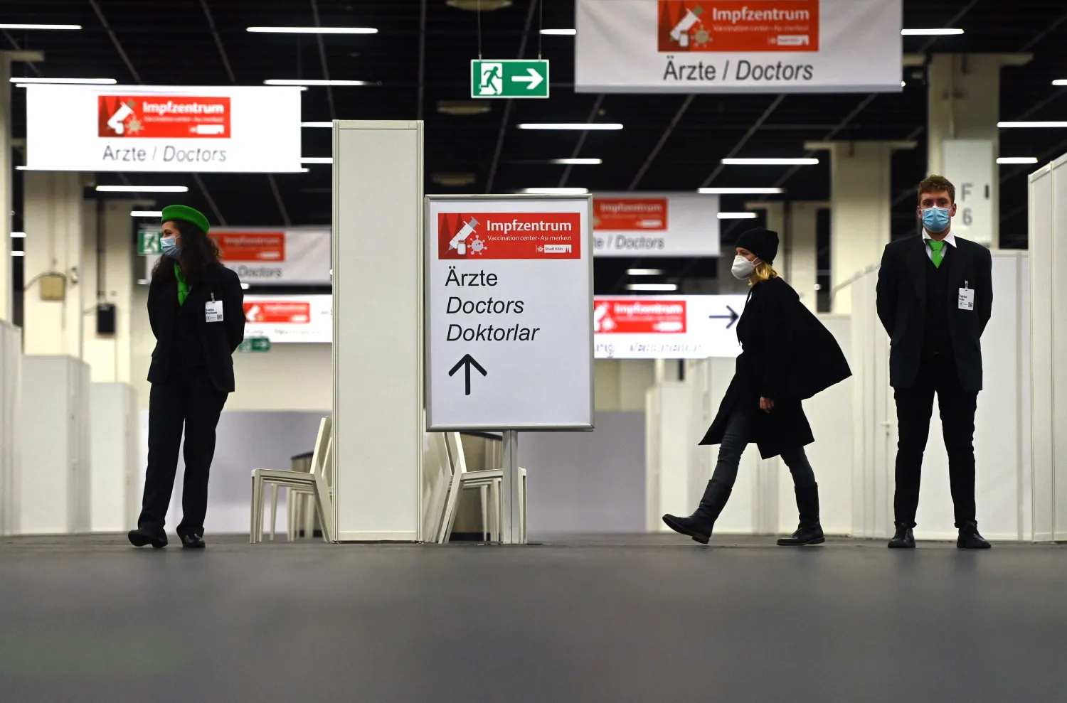 أشخاص يرتدون أقنعة واقية للوجه ويمشون في قاعة مركز التطعيم ضد فيروس «كورونا» خلال إجراء اختبار في كولونيا (أ.ف.ب)