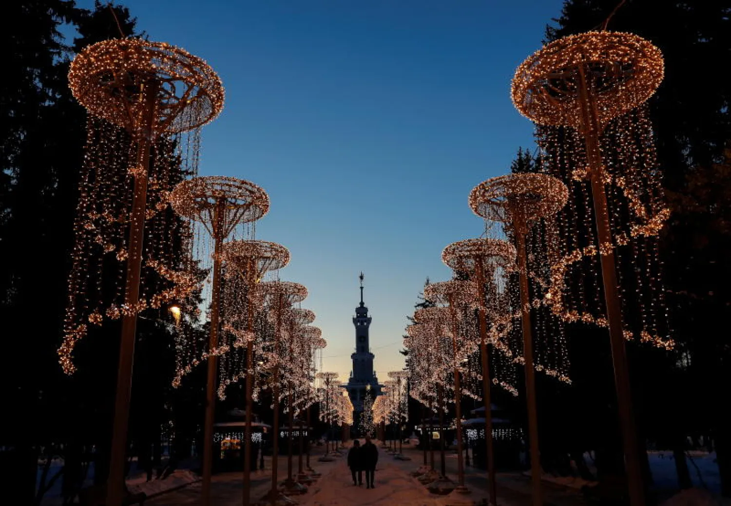 روسيان في أحد شوارع موسكو المزيّنة بأضواء نهاية السنة (رويترز)