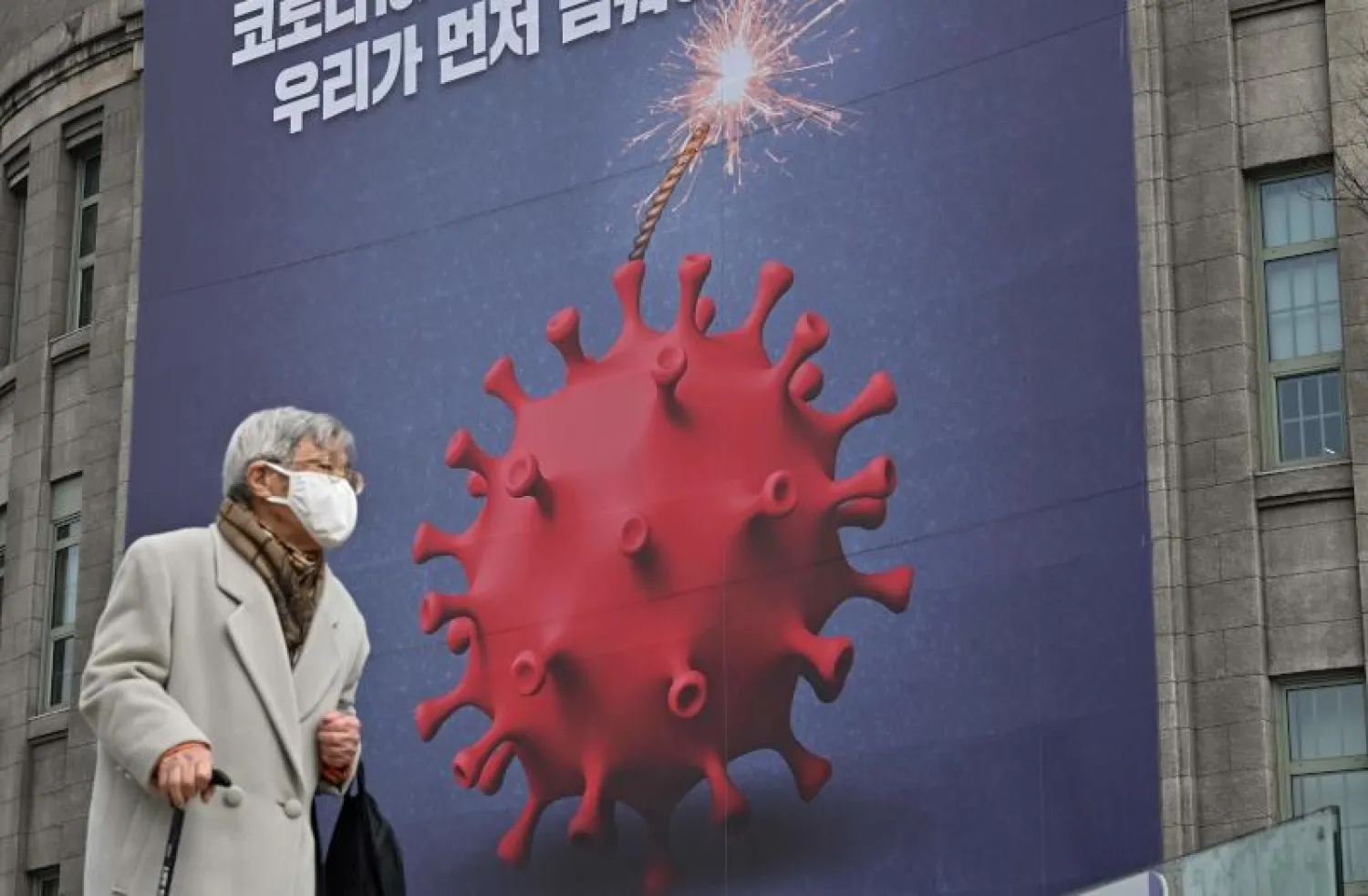 امرأة مسنة تمر بجانب صورة تصوّر فيروس كورونا كقنبلة للتحذير من «كوفيد 19» في سيول (أ.ف.ب)