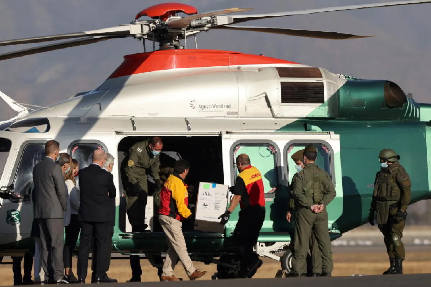 نقل صندوق يحوي لقاحات «فايزر/بايونتك» إلى طائرة مروحية في مطار سانتياغو عاصمة تشيلي، في حضور رئيس البلاد سيباستيان بينيرا (رويترز)