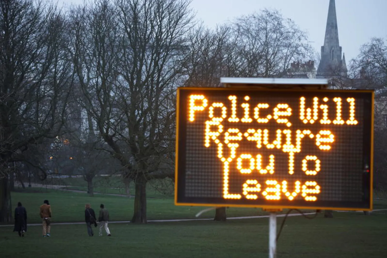 أشخاص يسيرون بالقرب من لافتة تحذيرية من التجمعات (رويترز)