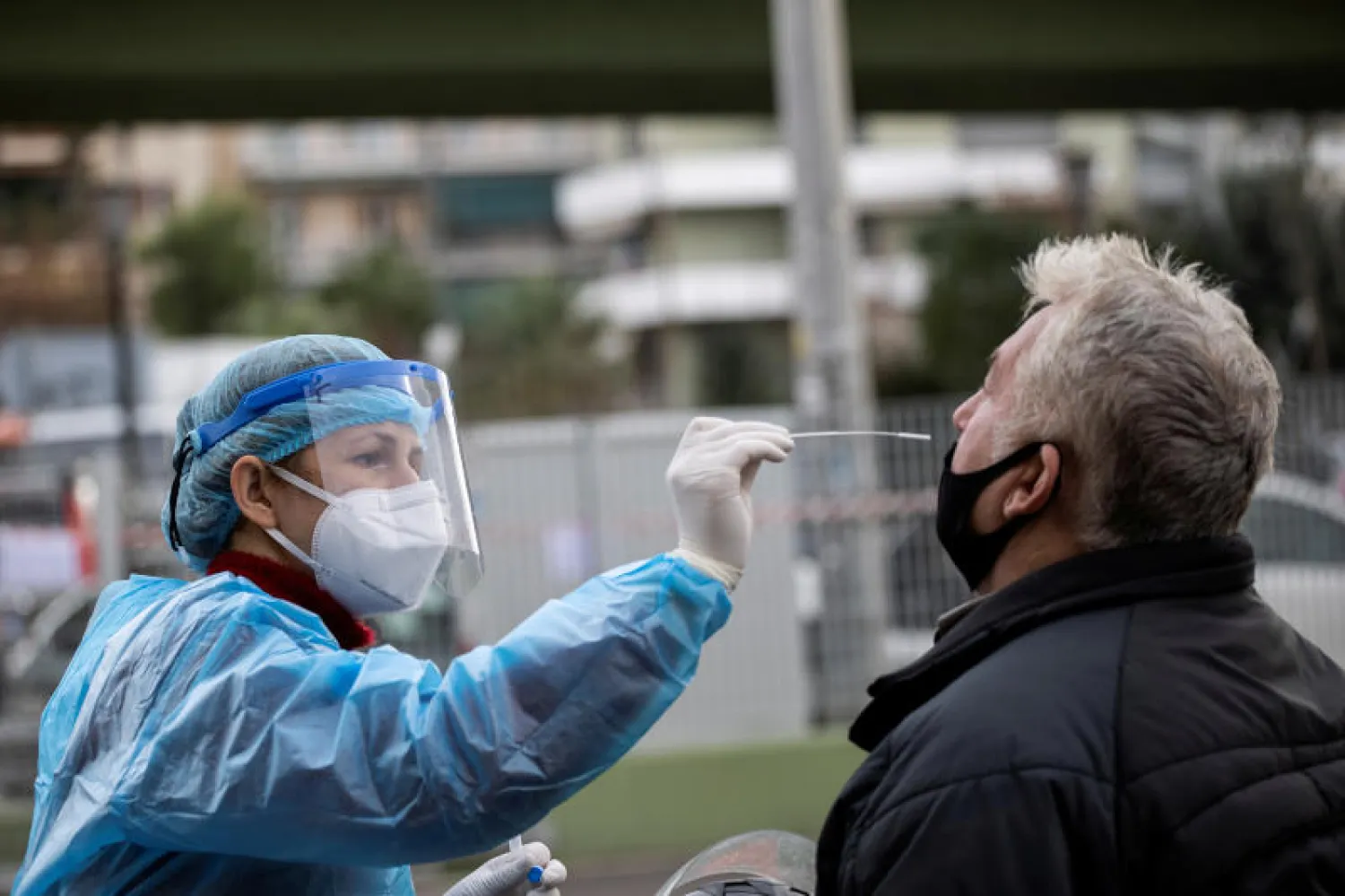 عامل صحي يجري الفحص السريع لكشف كورونا لرجل في أثينا (رويترز)