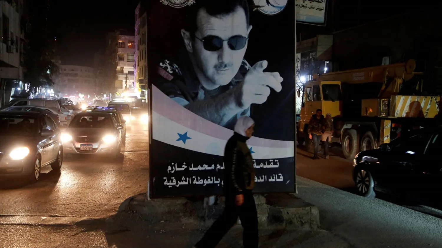A woman walks past a poster depicting Syria's president Bashar Assad in Damascus, Syria, March 5, 2020. (Reuters)