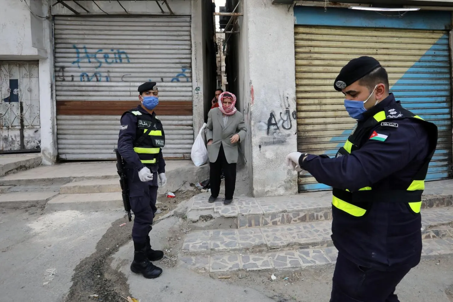 Jordanian police officers stand guard as a man waits to get bread in a closed-down part of Al-Nasr area, amid the coronavirus disease (COVID-19) outbreak, in Amman, Jordan, April 15, 2020. REUTERS/Muhammad Hamed