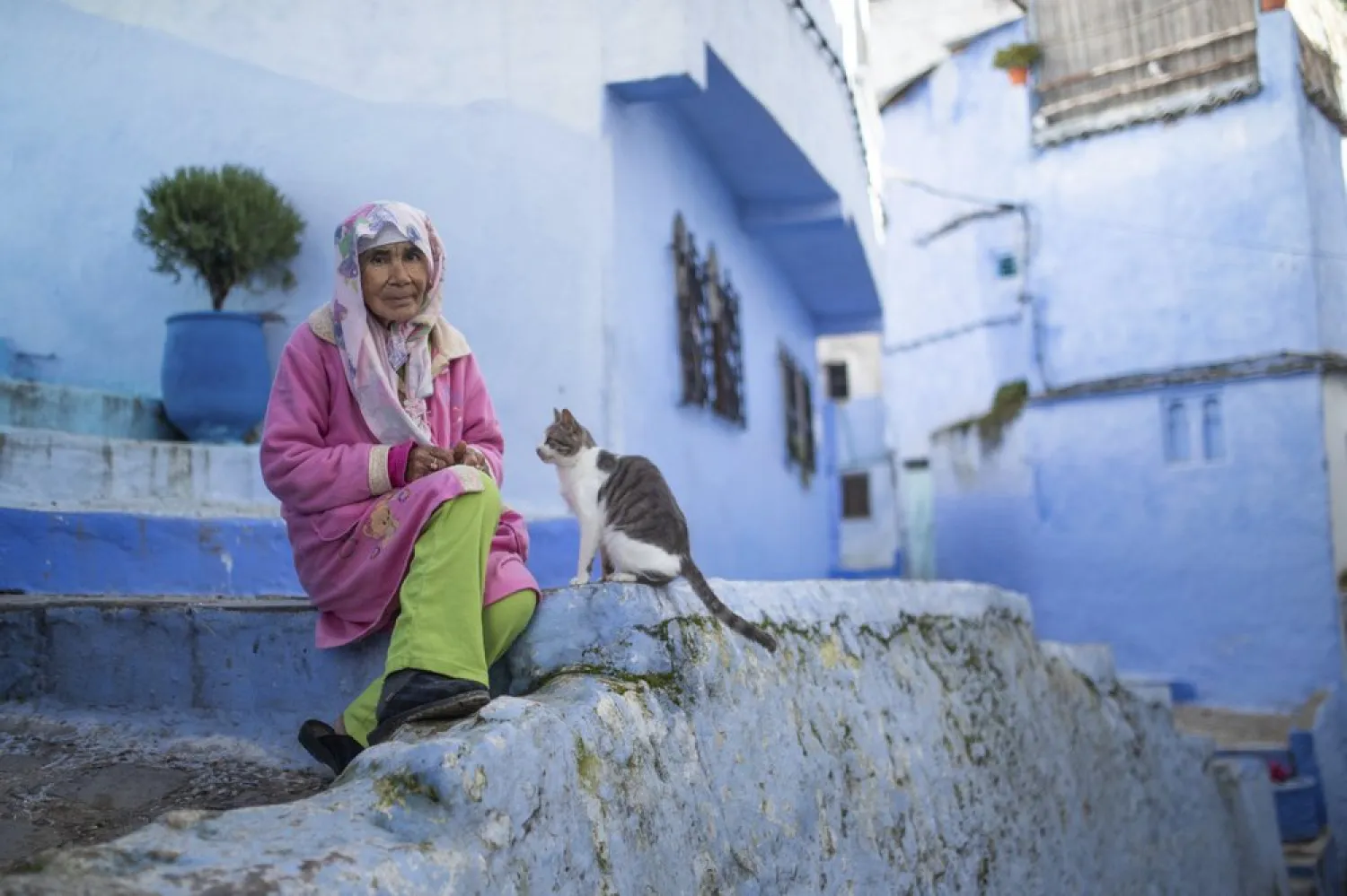 An elderly lady sits next to her cat outside her home in an alleyway deserted of tourists in Chefchaouen, northern Morocco, Saturday, Dec. 26, 2020. (AP)