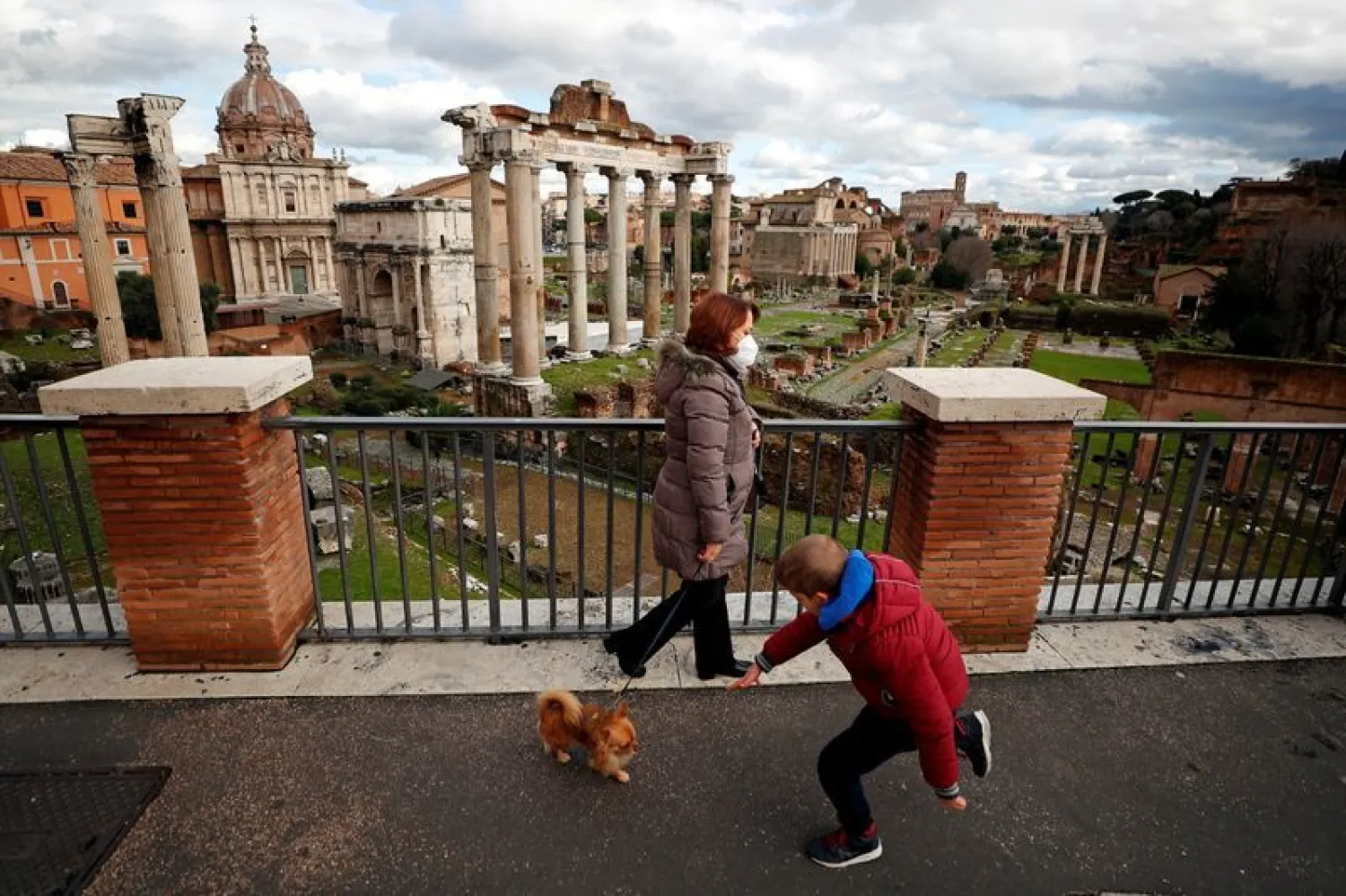 A woman wearing a protective face mask walks her dog near the Roman Forum, one day before the country goes back to lockdown as part of the efforts put in place to curb the spread of the coronavirus disease (COVID-19), in Rome, Italy, January 4, 2021. REUTERS/Guglielmo Mangiapane/File Photo