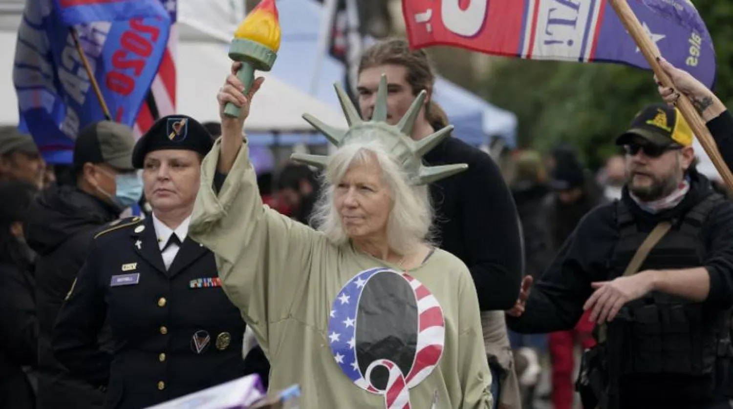 زن مشعل به دست در اعتراضات روز چهاشنبه واشنگتن بلوزی با علامت جنبش کیو پوشیده است (آسوشیتد پرس)