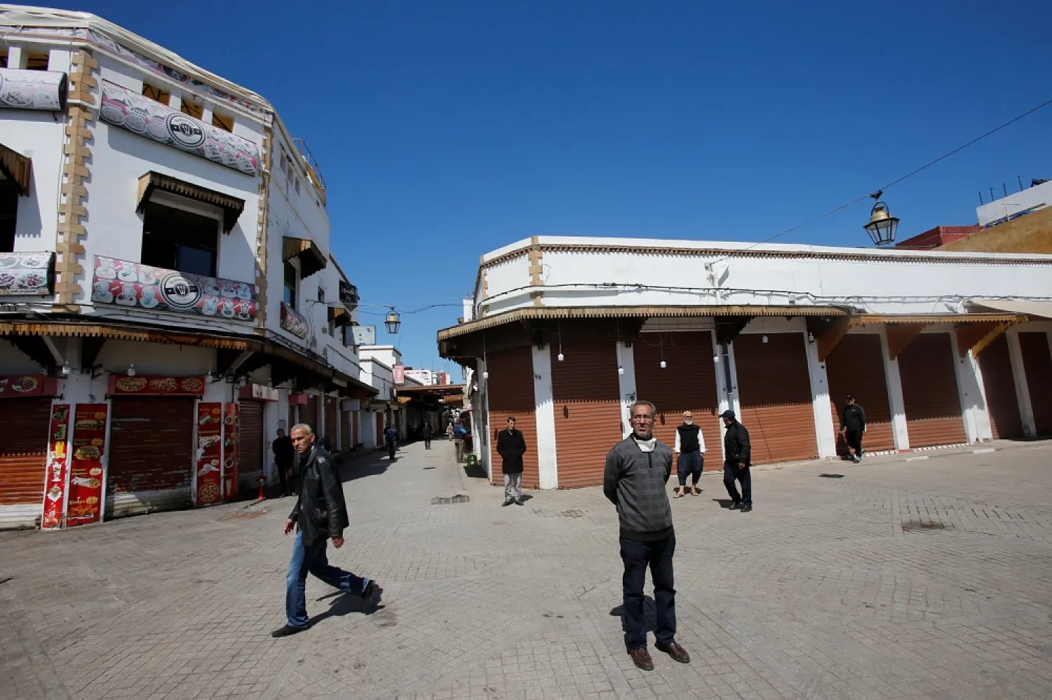 People stand near an empty street with closed shops in the old city, following the coronavirus disease (COVID-19) outbreak in Rabat, Morocco March 23, 2020. (Reuters)