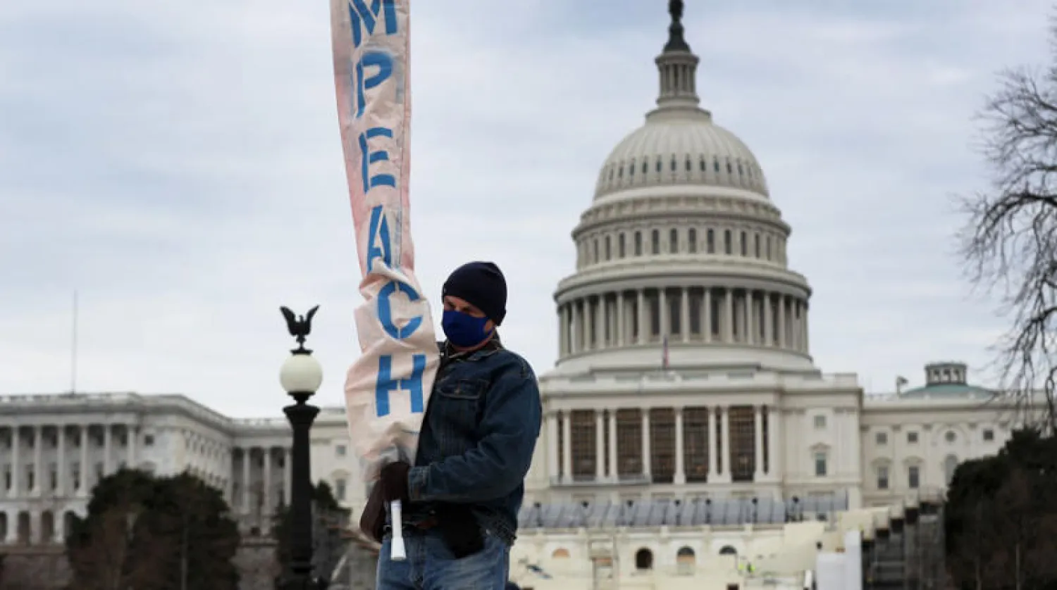 أميركي يحمل لافتة تدعو إلى عزل الرئيس ترمب خارج مبنى الكابيتول (أ.ف.ب)