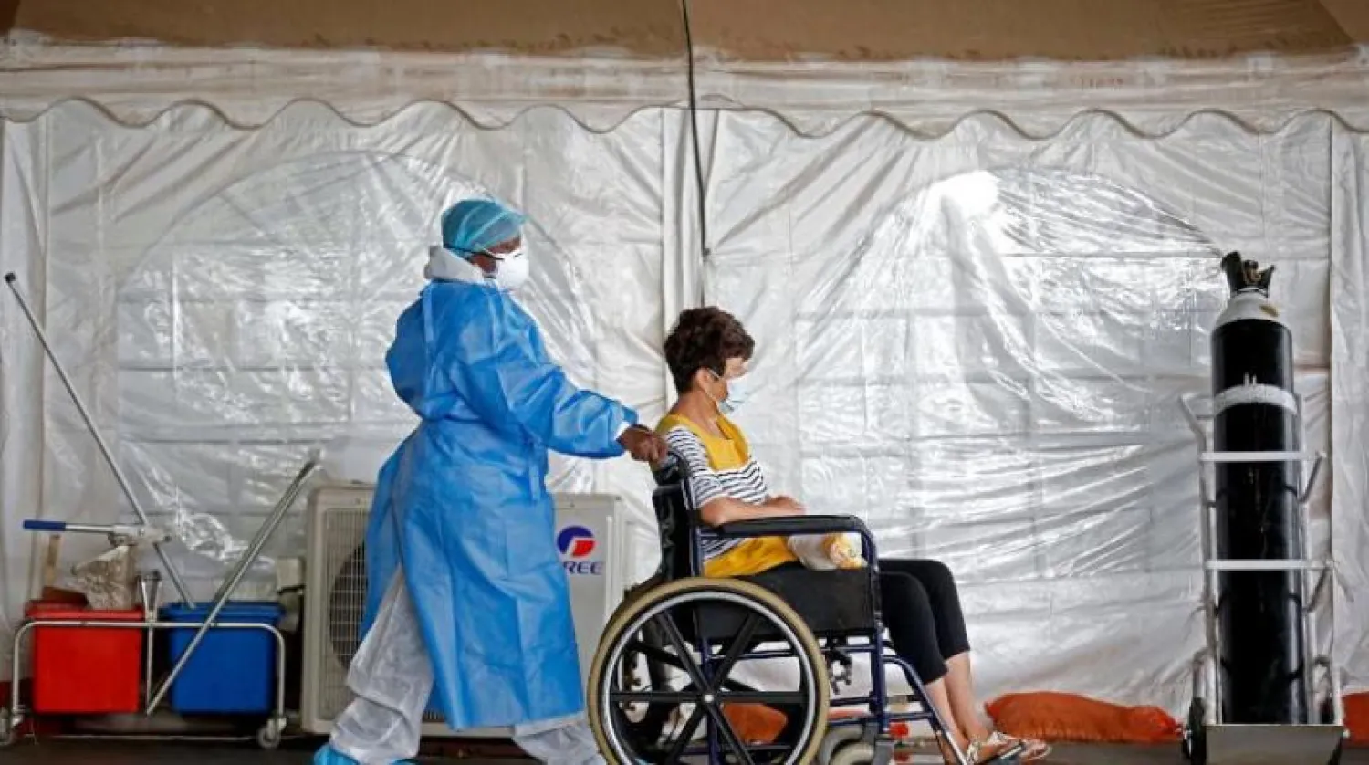 Güney Afrika’daki bir sağlık çalışanı tekerlekli sandalyedeki koronavirüs hastasıyla ilgileniyor (AFP)