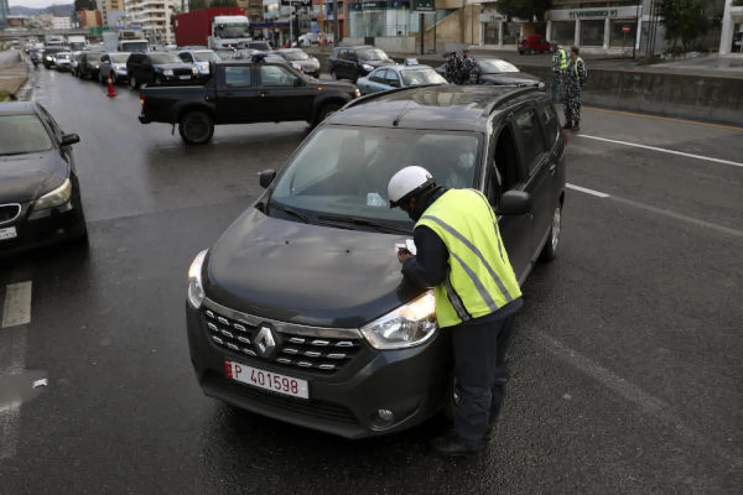 A police officer issues fines to owners of vehicles that violate the lockdown, in Beirut, Lebanon, Thursday, Jan. 14, 2021. Lebanese authorities began enforcing an 11-day nationwide shutdown and round the clock curfew Thursday, hoping to limit the spread of coronavirus infections spinning out of control after the holiday period. (AP Photo/Bilal Hussein)
