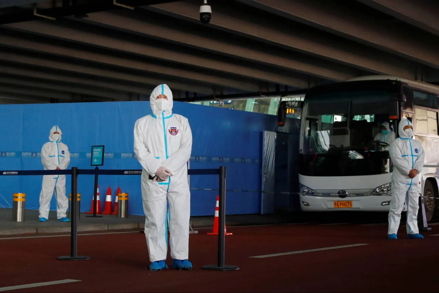 Staff members in protective suits stand guard next to a bus before the expected arrival of a World Health Organization (WHO) team tasked with investigating the origins of the coronavirus disease (COVID-19) pandemic, at Wuhan Tianhe International Airport in Wuhan, Hubei province, China January 14, 2021. REUTERS/Thomas Peter