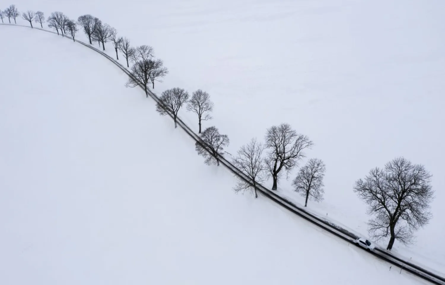 A car drives on a snowy road through the Ore Mountains in Einsiedel, Germany, Thursday, Jan. 14, 2021. A snow front that passed through during the night has brought plenty of new snow. ( Jan Woitas/dpa via AP)