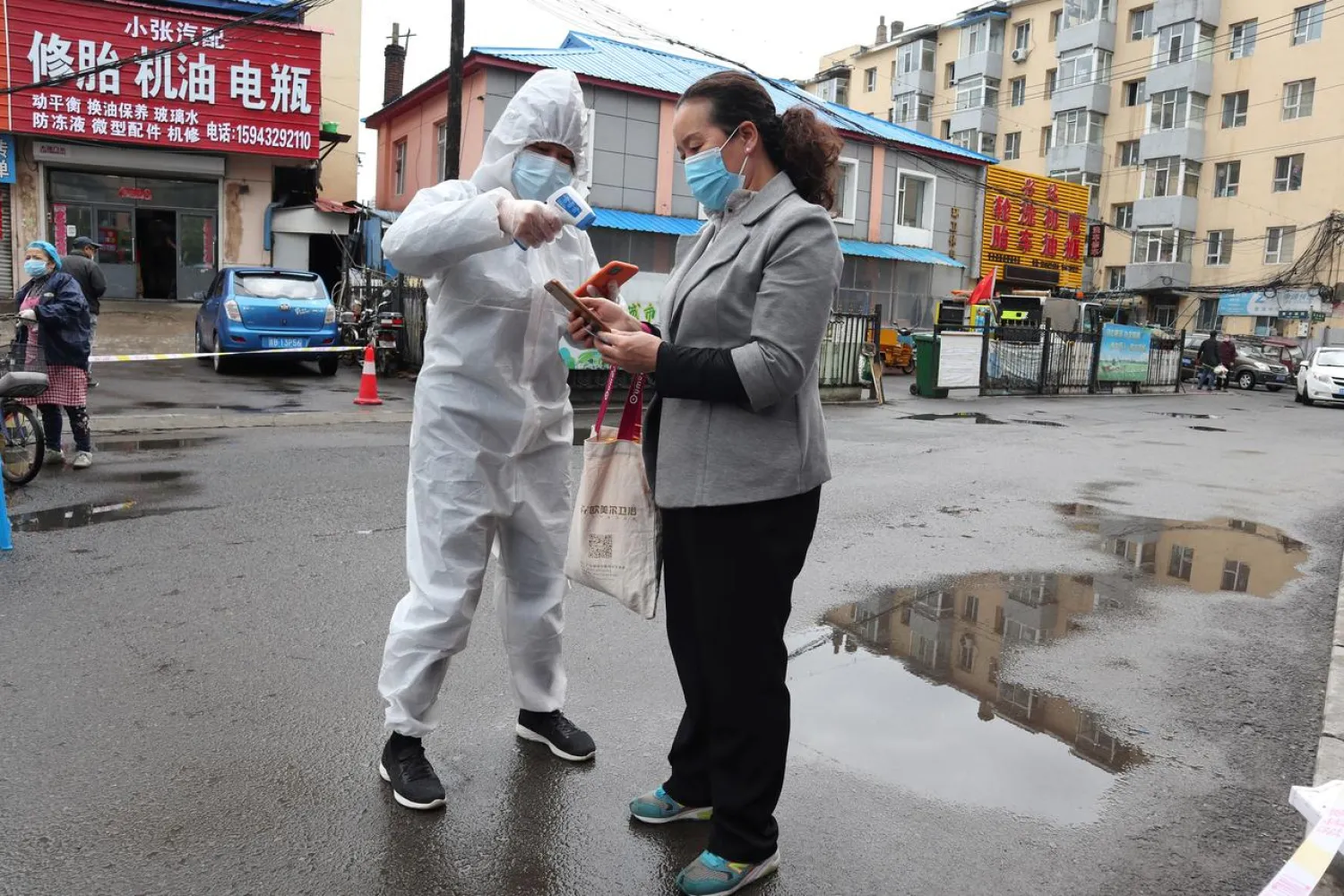 A worker in protective suit takes body temperature measurement of a woman following the coronavirus disease (COVID-19) outbreak in Jilin, Jilin province, China May 17, 2020. cnsphoto via REUTERS