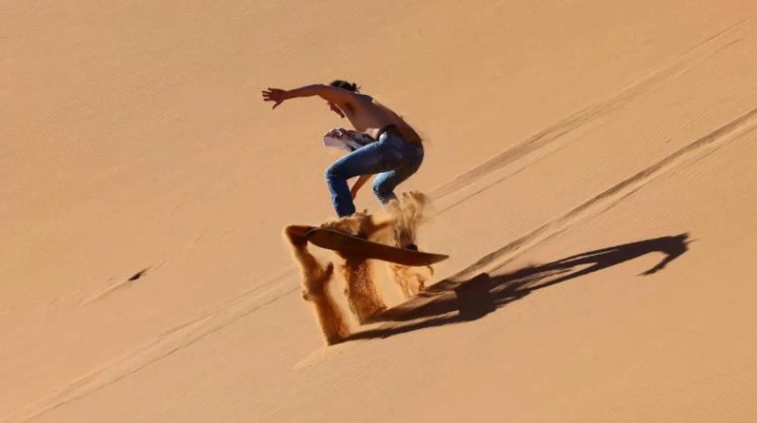 A tourist practices sandboarding in the Dubai desert in the United Arab Emirates, on January 11, 2021. (Photo by GIUSEPPE CACACE / AFP)