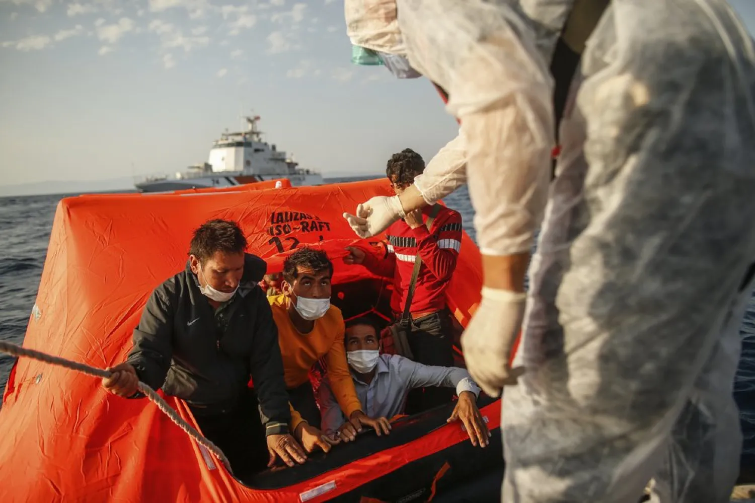 Turkish coast guards officers on their vessel, wearing protective gear to help prevent the spread of coronavirus, talk to migrants on a life raft during a rescue operation in the Aegean Sea, between Turkey and Greece, Saturday, Sept. 12, 2020. (AP Photo/Emrah Gurel)
