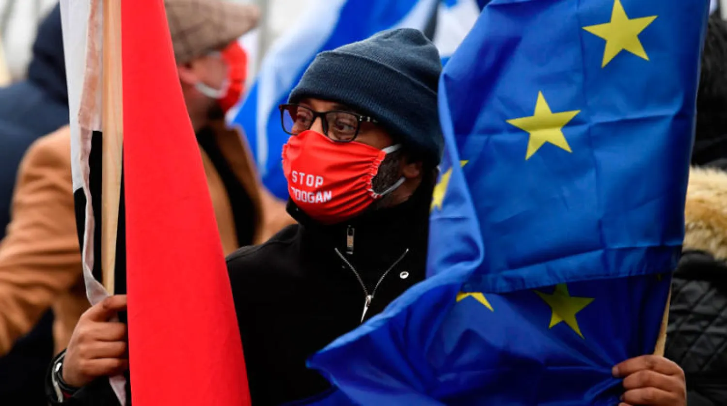 متظاهر يرتدي قناعاً كُتب عليه «أوقفوا إردوغان» خلال مظاهرة أمام مقر البرلمان الأوروبي في بروكسل أمس (أ.ف.ب)