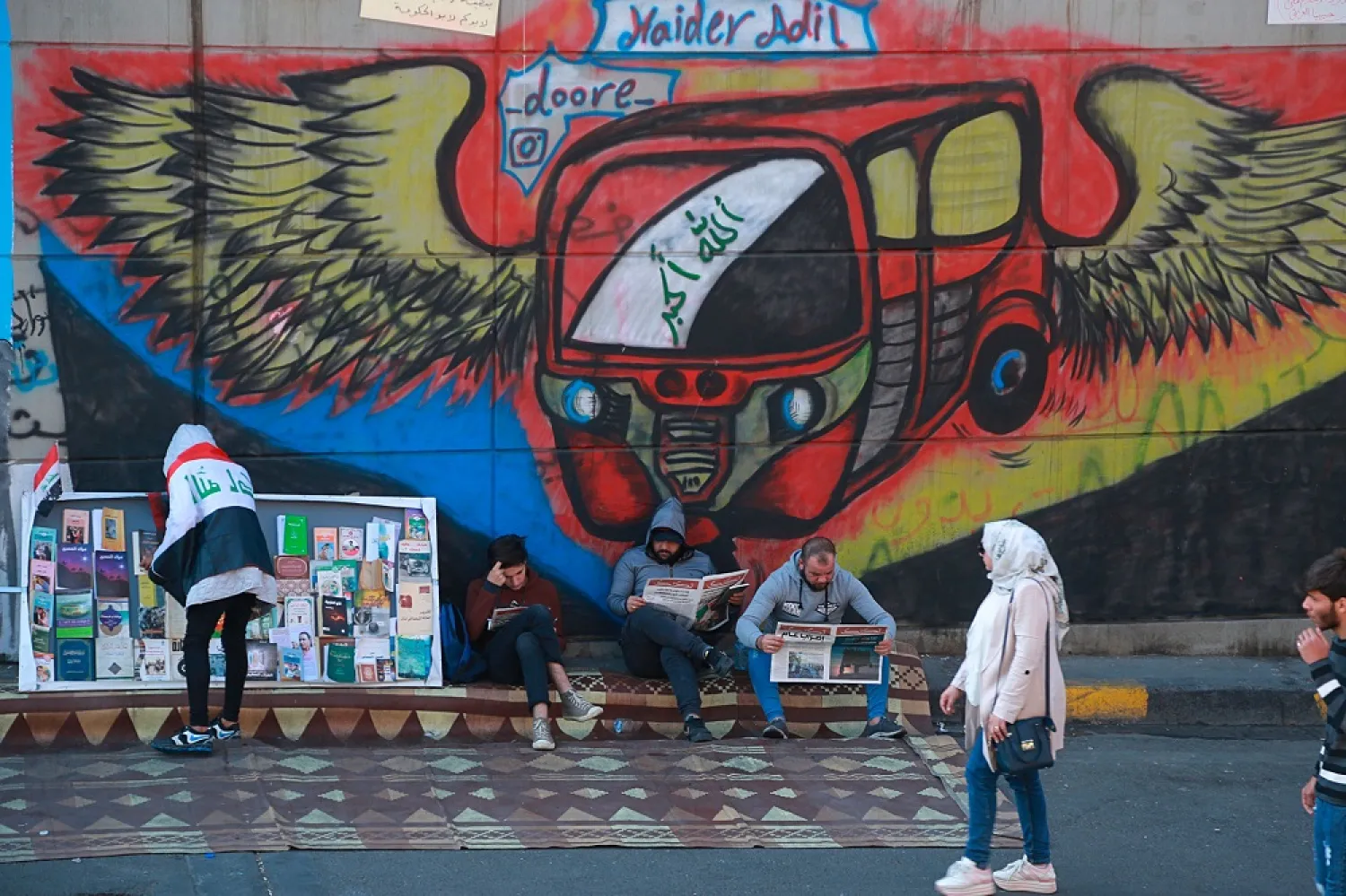 Protesters read copies of newspapers in front of graffiti in Tahrir Square, Baghdad, Iraq, November 20, 2019. (AP)