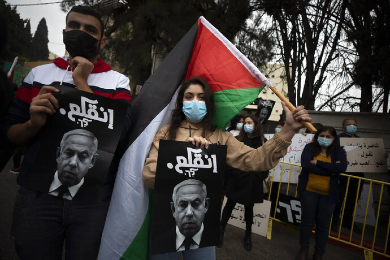 Palestinian protesters hold signs and flags during a demonstration against a visit of Israeli Prime Minister Benjamin Netanyahu to the northern Arab city of Nazareth, Israel, Wednesday, Jan. 13, 2021. Netanyahu, who has spent much of his long career casting Israel's Arab minority as a potential fifth column led by terrorist sympathizers, is now openly courting their support as he seeks reelection in the country's fourth vote in less than two years. (AP Photo/Sebastian Scheiner)