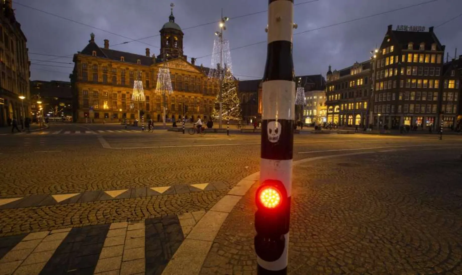 In this Tuesday Dec. 15, 2020, file photo, A skull is glued onto a traffic light on the near-empty Dam Square with the Royal Palace, seen center rear, in Amsterdam, Netherlands. The Dutch government said Wednesday, Jan. 20, 2021, that it wants to impose a curfew as part of beefed-up restrictions to rein in the spread of new more contagious variants of the coronavirus that already accounts for at least one in every 10 Dutch infections.(AP Photo/Peter Dejong, File)