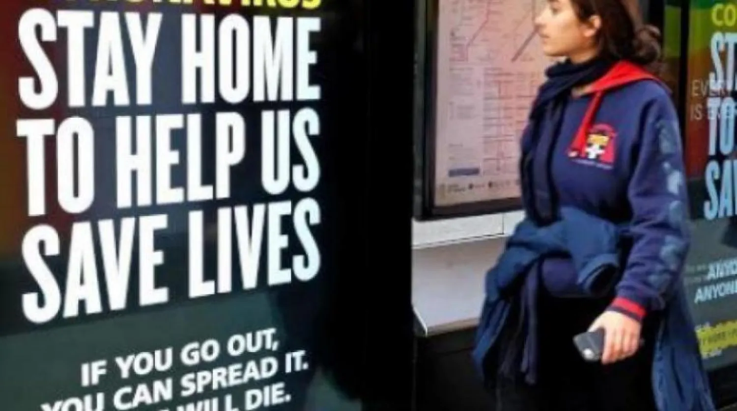 Londra’da koronavirüs ile mücadele kapsamında evde kalmaya çağıran bir tabelanın önünde yürüyen genç kız (AFP)