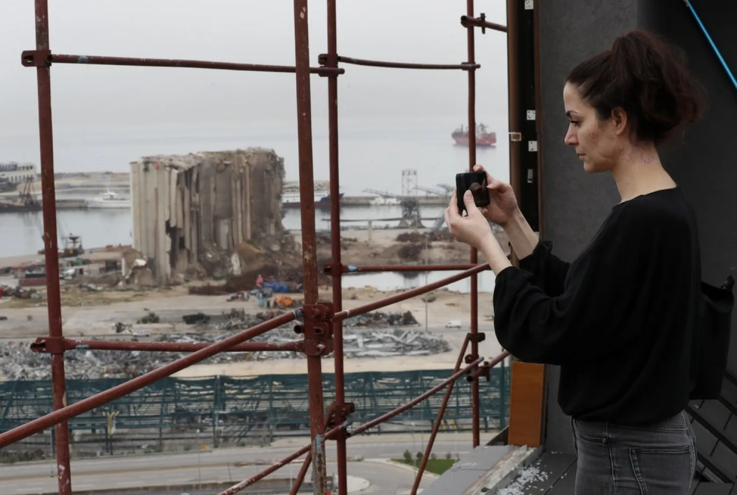 Joana Dagher takes pictures of the scene of the Beirut port blast from her damaged apartment rooftop, in Beirut, Lebanon, Jan. 27, 2021. (AP)