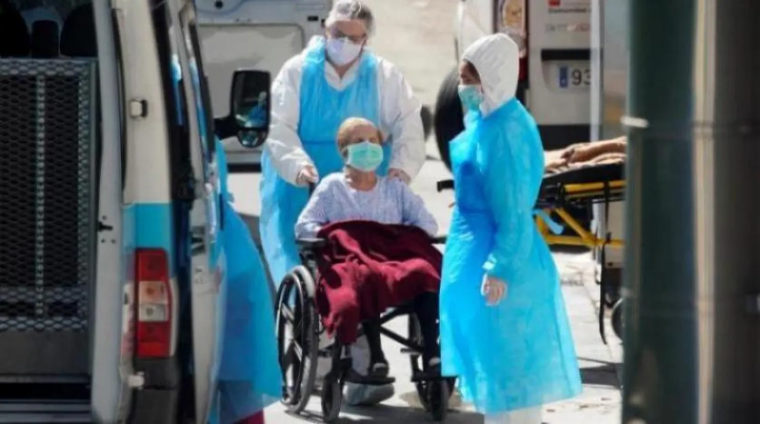 Madrid yakınlarındaki Leganes’te iki sağlık personeli koronavirüslü bir kişinin tekerlekli sandalyesini itiyor (Reuters)