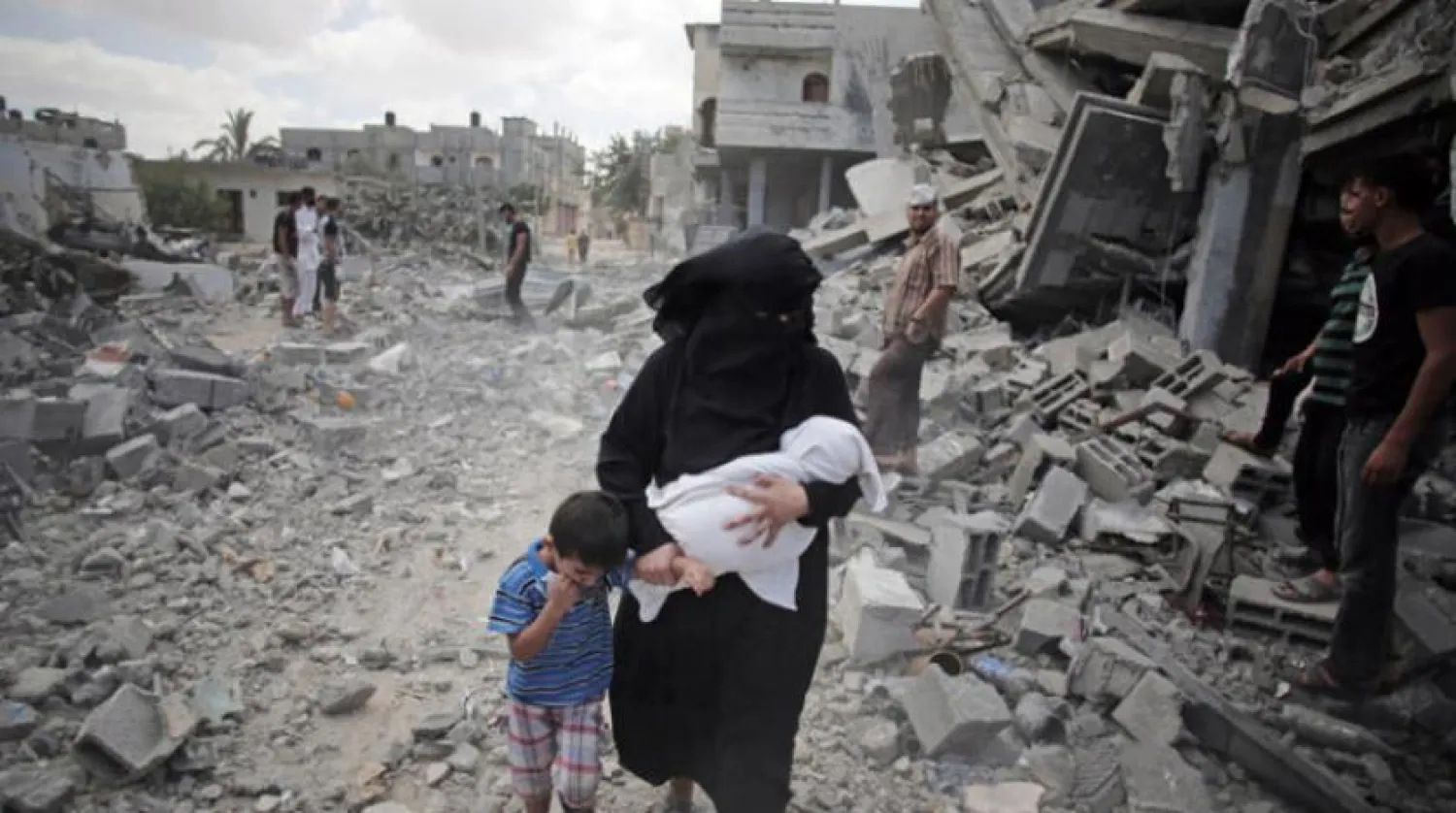 FILE - In this Aug. 4, 2014 photo, a Palestinian woman passes by rescuers inspecting the rubble of destroyed houses following Israeli strikes in Rafah refugee camp, southern Gaza Strip. (AP Photo/Khalil Hamra, File)