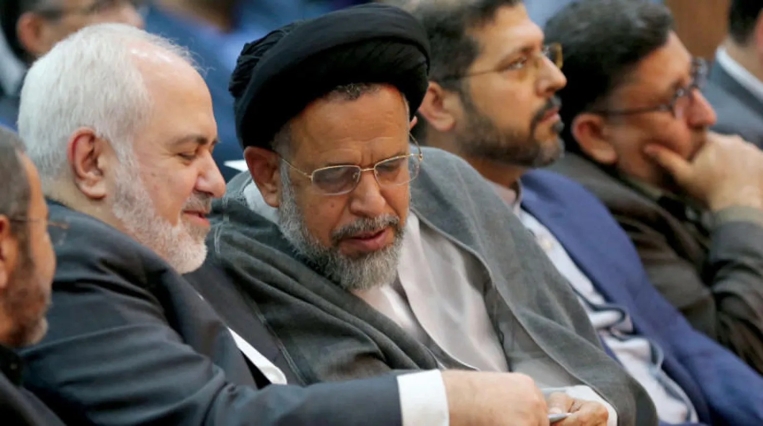 وزير الأمن محمود علوي ينظر إلى هاتف جوال بيد وزير الخارجية محمد جواد ظريف الذي يغطي جزءاً من الشاشة بأصبعه خلال مناسبة جامعية بطهران في أكتوبر 2019 (أ.ف.ب)