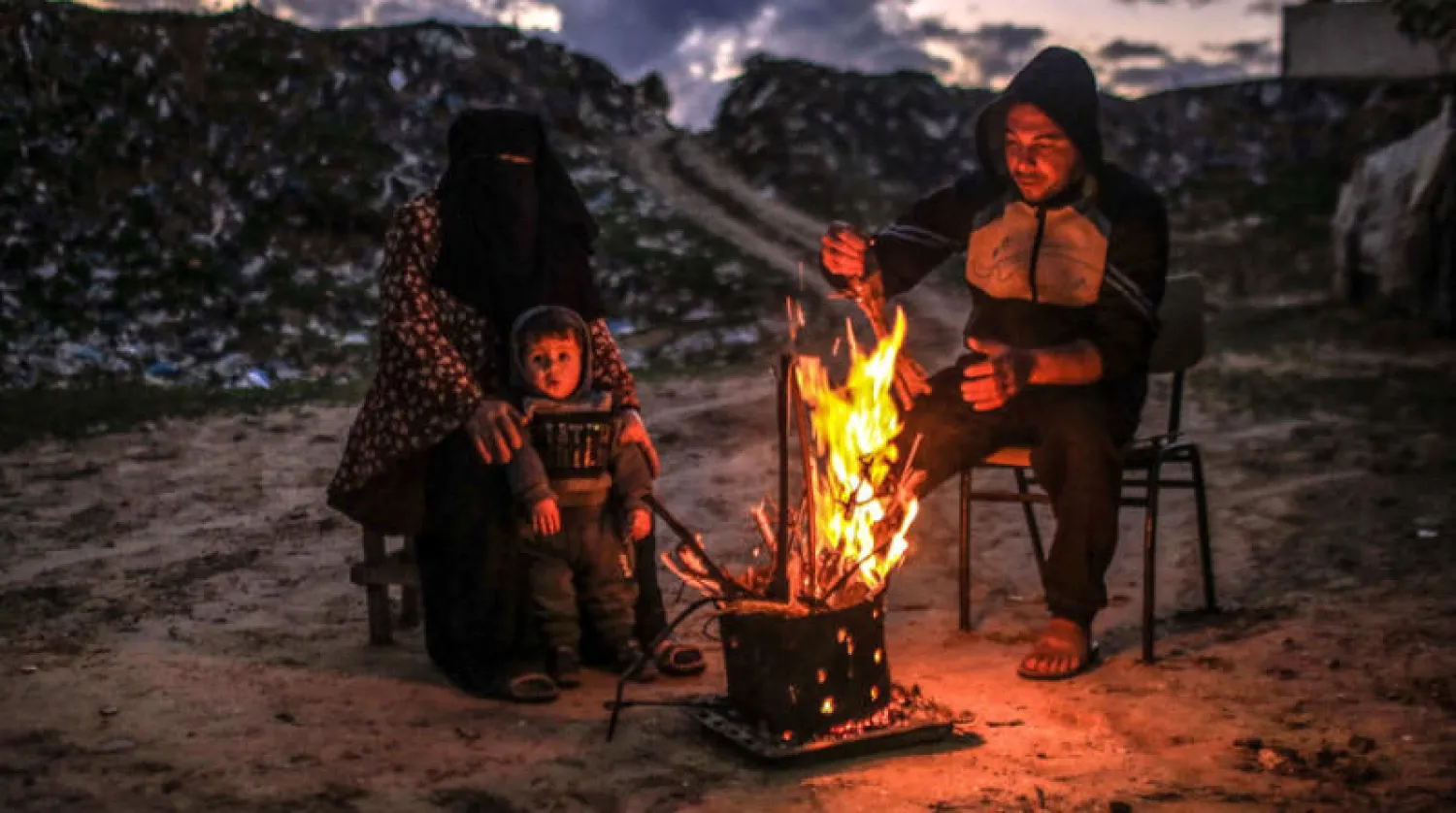 عائلة فلسطينية تستخدم الحطب للتدفئة في مخيم للاجئين بخان يونس يوم الجمعة في ظل موجة برد تضرب قطاع غزة (إ.ب.أ)