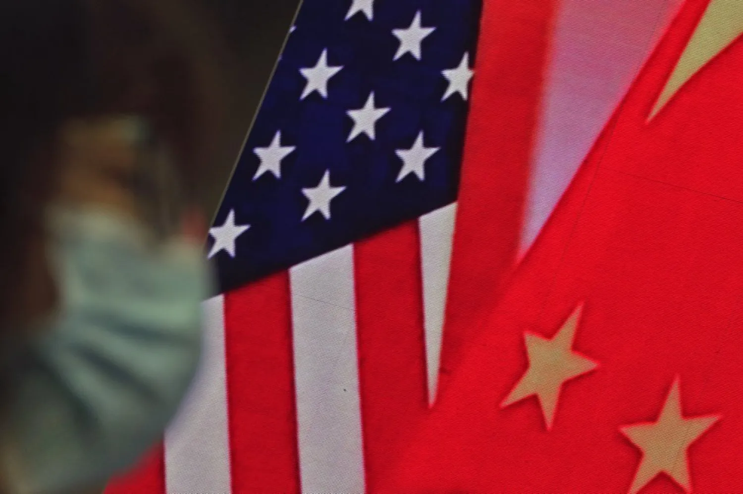 A woman wearing a face mask sits near a screen showing China and US flags as she listens to a speech by Chinese Foreign Minister Wang Yi at the Lanting Forum, in Beijing Feb. 22, 2021. (AP)