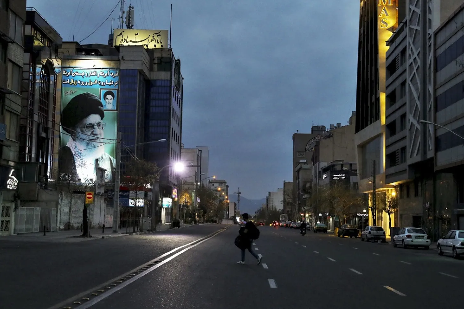 In this March 24, 2020 photo, a pedestrian crosses an empty street with a portrait of Iran's Supreme Leader Ali Khamenei, in Tehran, Iran. (AP)