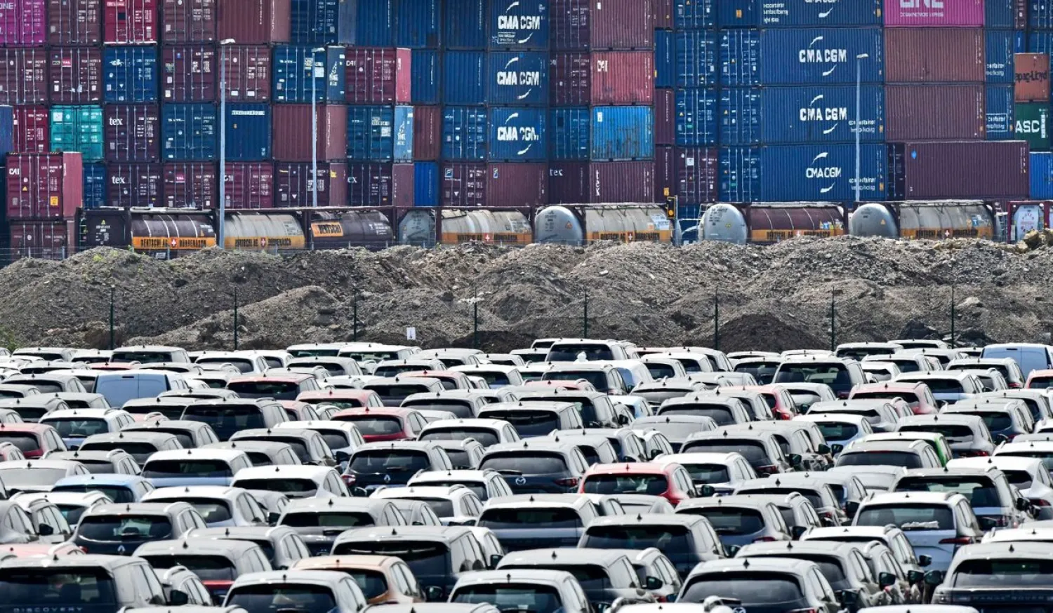 In this Wednesday, June 3, 2020 photo new cars are stored in front of containers at the 'logport' (logistic port) in Duisburg, Germany. (AP Photo/Martin Meissner, file)