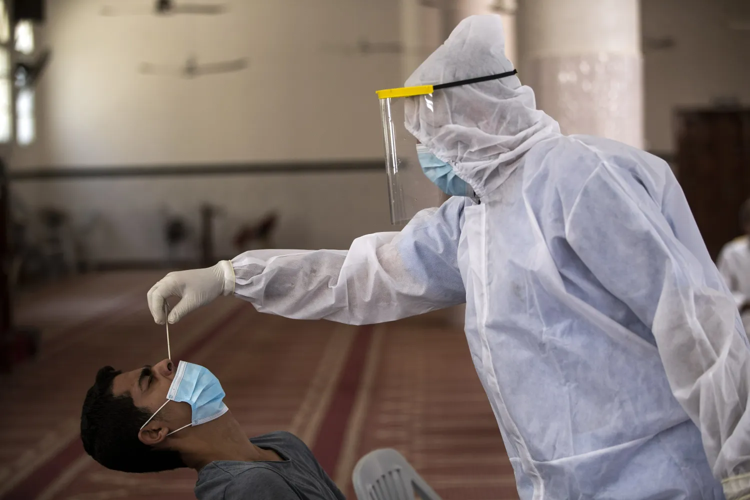 FILE - In this Sept. 21, 2020 file photo, a Palestinian paramedic wearing a full protective suit, takes a nasal swab to test for COVID-19 from a man, at a mosque in Gaza City. (AP Photo/Khalil Hamra, File)