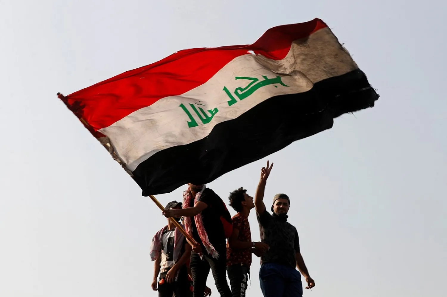 A demonstrator holds an Iraqi flag as another gestures while they gather to mark the first anniversary of the anti-government protests in Baghdad, Iraq October 25, 2020. (Reuters)