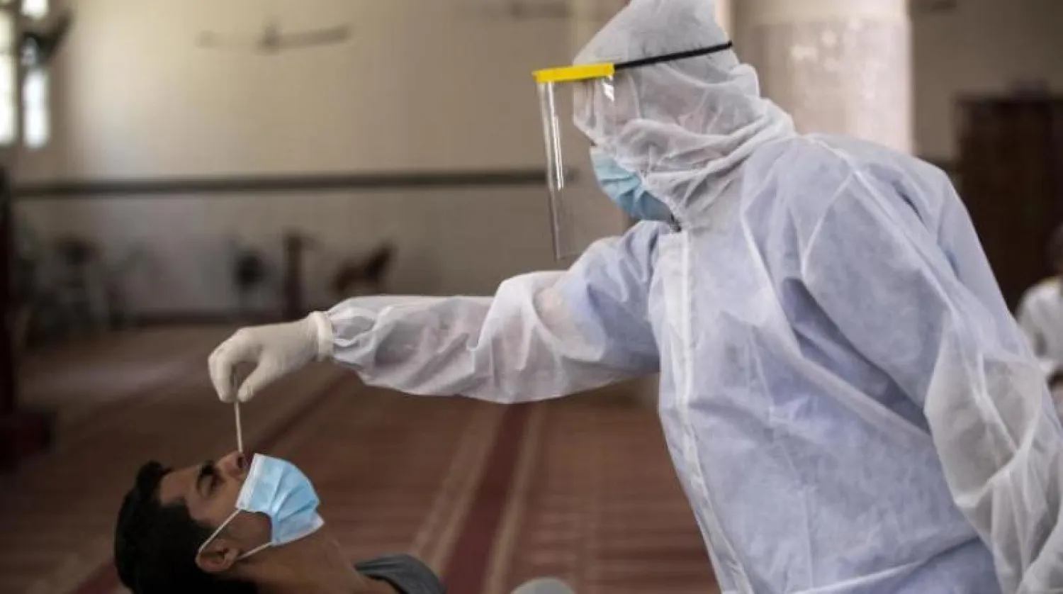 مسعف فلسطيني يرتدي بدلة واقية يأخذ مسحة أنف من رجل في مسجد بمدينة غزة (أ.ب)