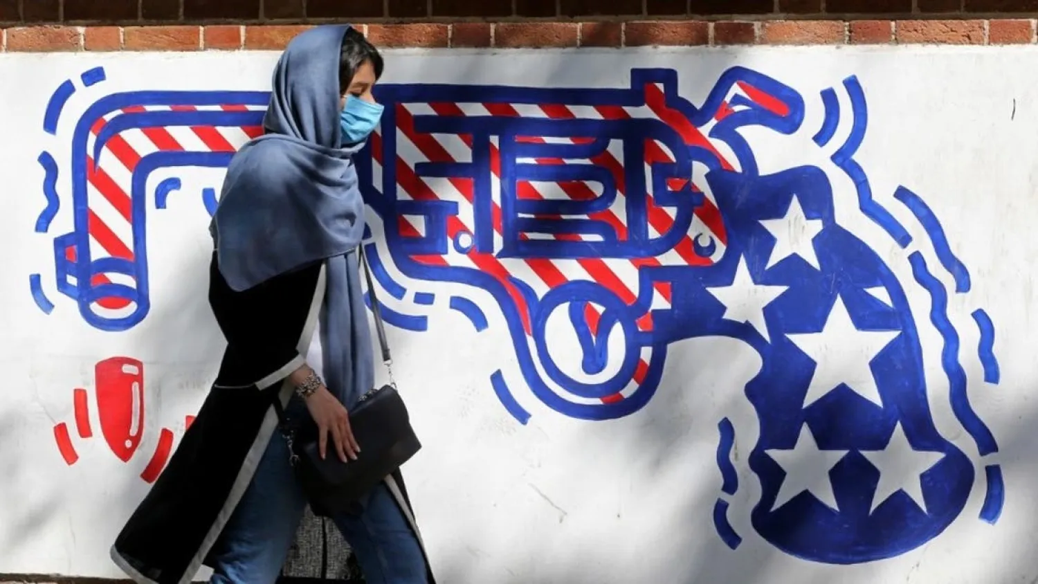A woman, wearing a protective mask amid the COVID-19 pandemic, walks past a mural painted on the outer walls of the former US embassy in the Iranian capital Tehran on September 20, 2020. (AFP)
