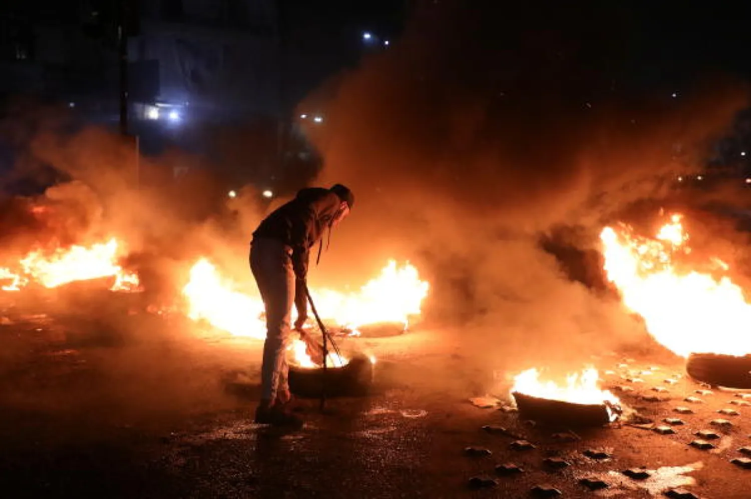 A demonstrator stands near burning tires during a protest against the fall in Lebanese pound currency and mounting economic hardship, in Beirut, Lebanon March 2, 2021. (Reuters)