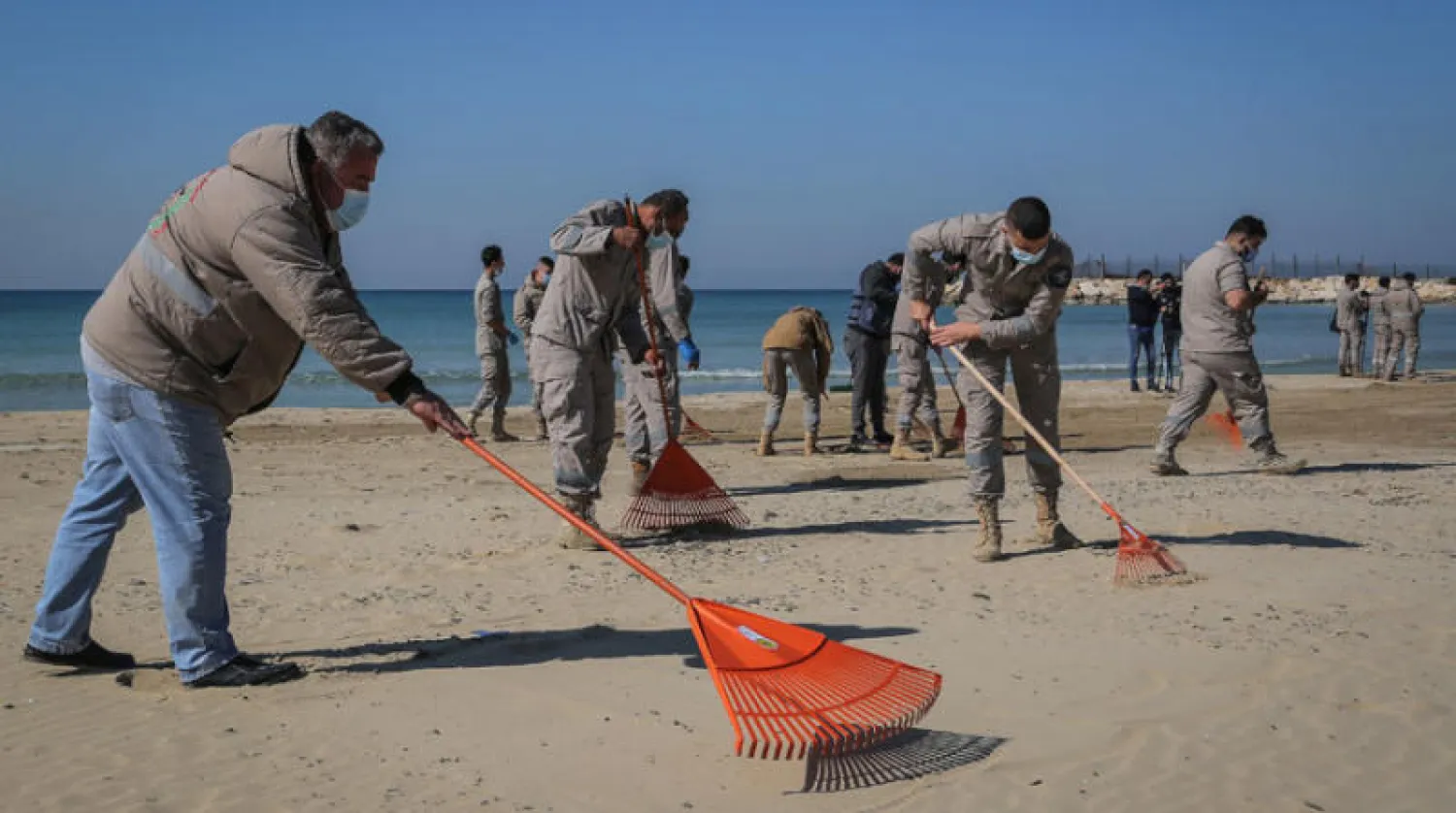 عمال ينظفون الشاطئ قرب مدينة صور بعد التسرب النفطي (د.ب.أ)