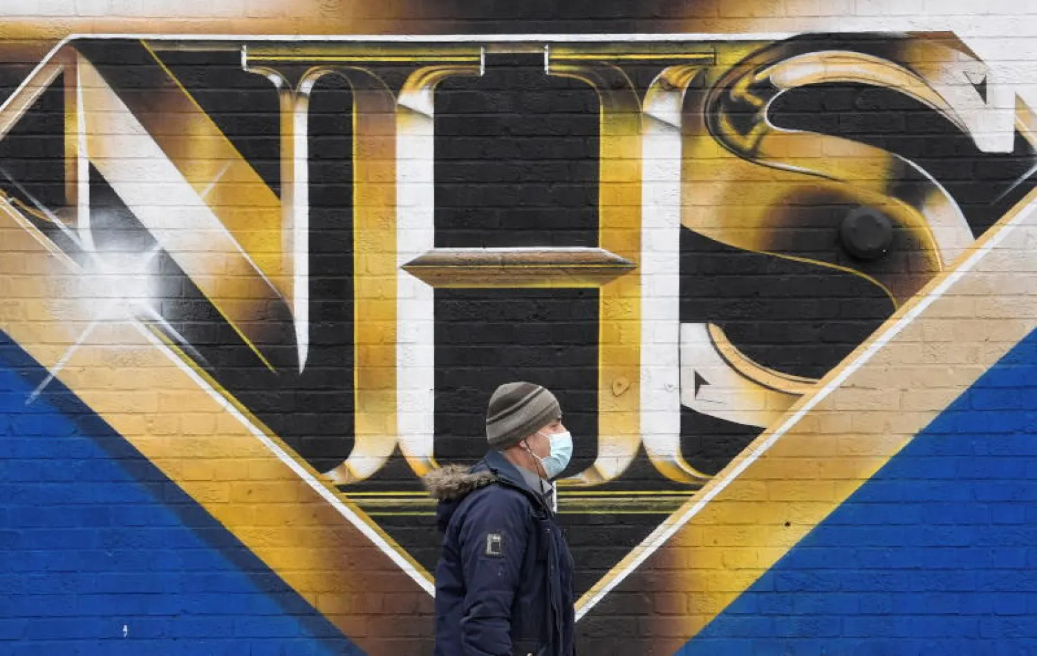 رجل يمر أمام ملصق لهيئة الخدمات الصحية البريطانية في لندن (رويترز)