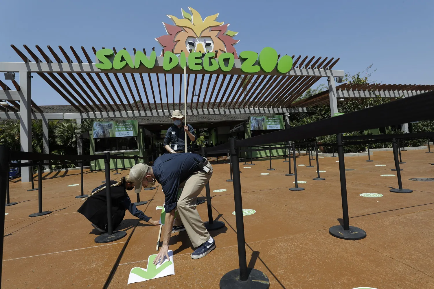 FILE - In this June 11, 2020, file photo, Devon Prince, front, puts down a sticker to guide visitors at the San Diego Zoo once it reopens, as Emmanuel Lopez, behind, and Ariel Hayes also work, in San Diego. (AP Photo/Gregory Bull, File)