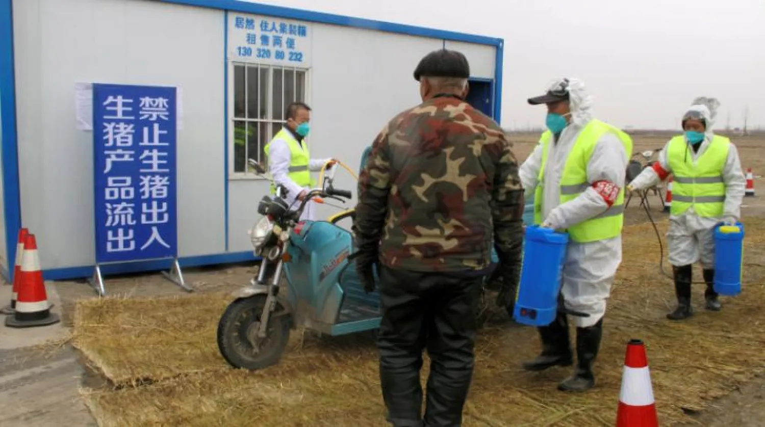 Koruyucu kıyafet giyen ekipler, Afrika domuz vebasının keşfedildiği çiftliğe giden yoldaki kontrol noktasında bir motosikleti dezenfekte ediyorlar (Reuters)