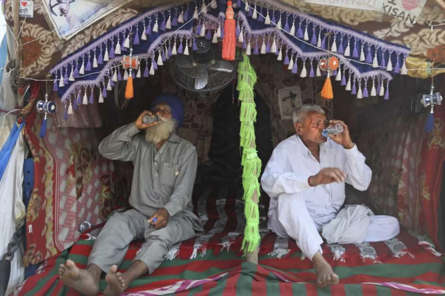 Indian farmers drink water sitting at the back of their tractor trolly as they camp at Singhu, along the Delhi-Haryana border, Friday, March 5, 2021. (AP Photo/Manish Swarup)