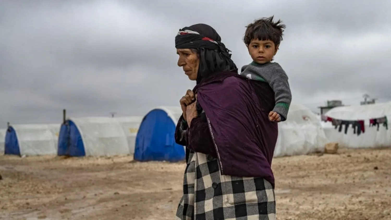 In this file photo taken on February 17, 2020, an elderly displaced Syrian woman carries a child in the Washukanni Camp for the internally displaced people near the predominantly Kurdish city of Hasakeh in northeastern Syria. (AFP)
