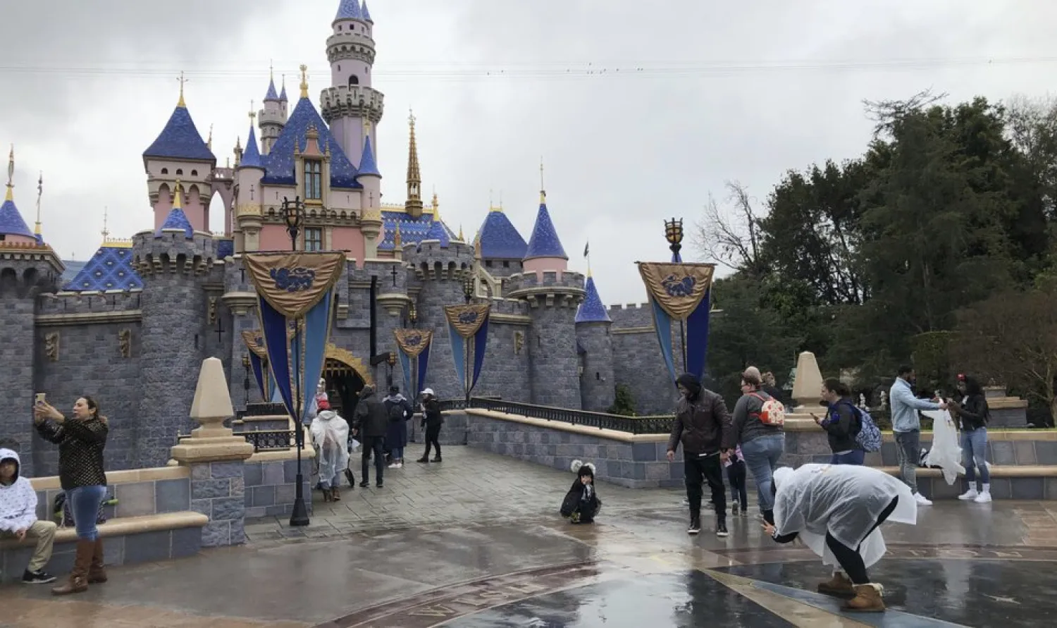 In this March 13, 2020, file photo, visitors take photos at Disneyland in Anaheim, Calif. California officials will allow people to attend Major League Baseball games and other sporting events, go to Disneyland, and watch live performances in limited capacities starting April 1, 2021. (AP Photo/Amy Taxin, File)