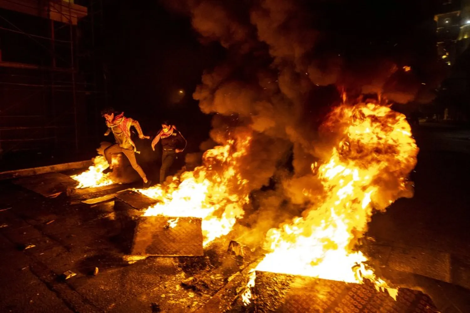 Protesters jump over burning tires that were set on fire to block a road, at Martyrs Square, in downtown Beirut, Lebanon, Saturday, March 6, 2021.  (AP Photo/Hassan Ammar)
