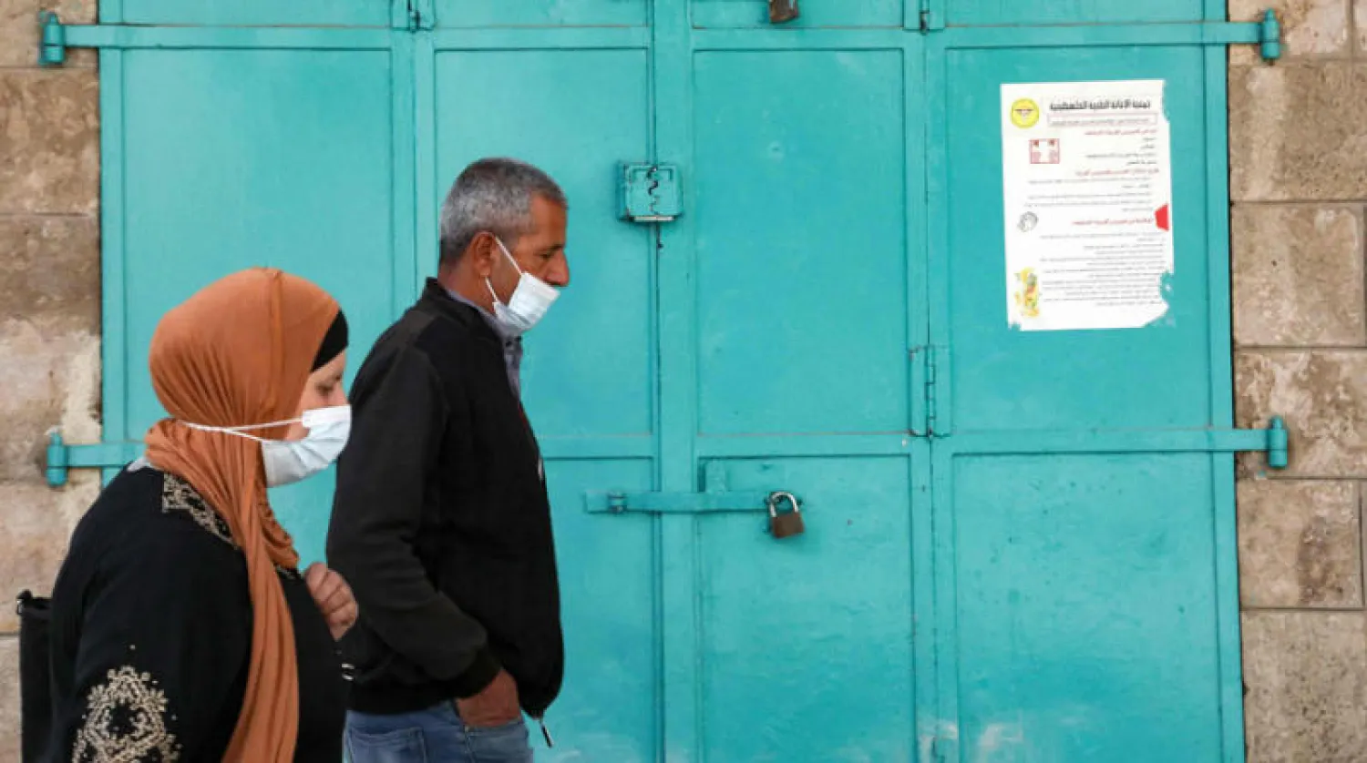 فلسطينيان يمران أمام محل تجاري مغلق بسبب تدابير «كورونا» في بيت لحم أمس (أ.ف.ب)