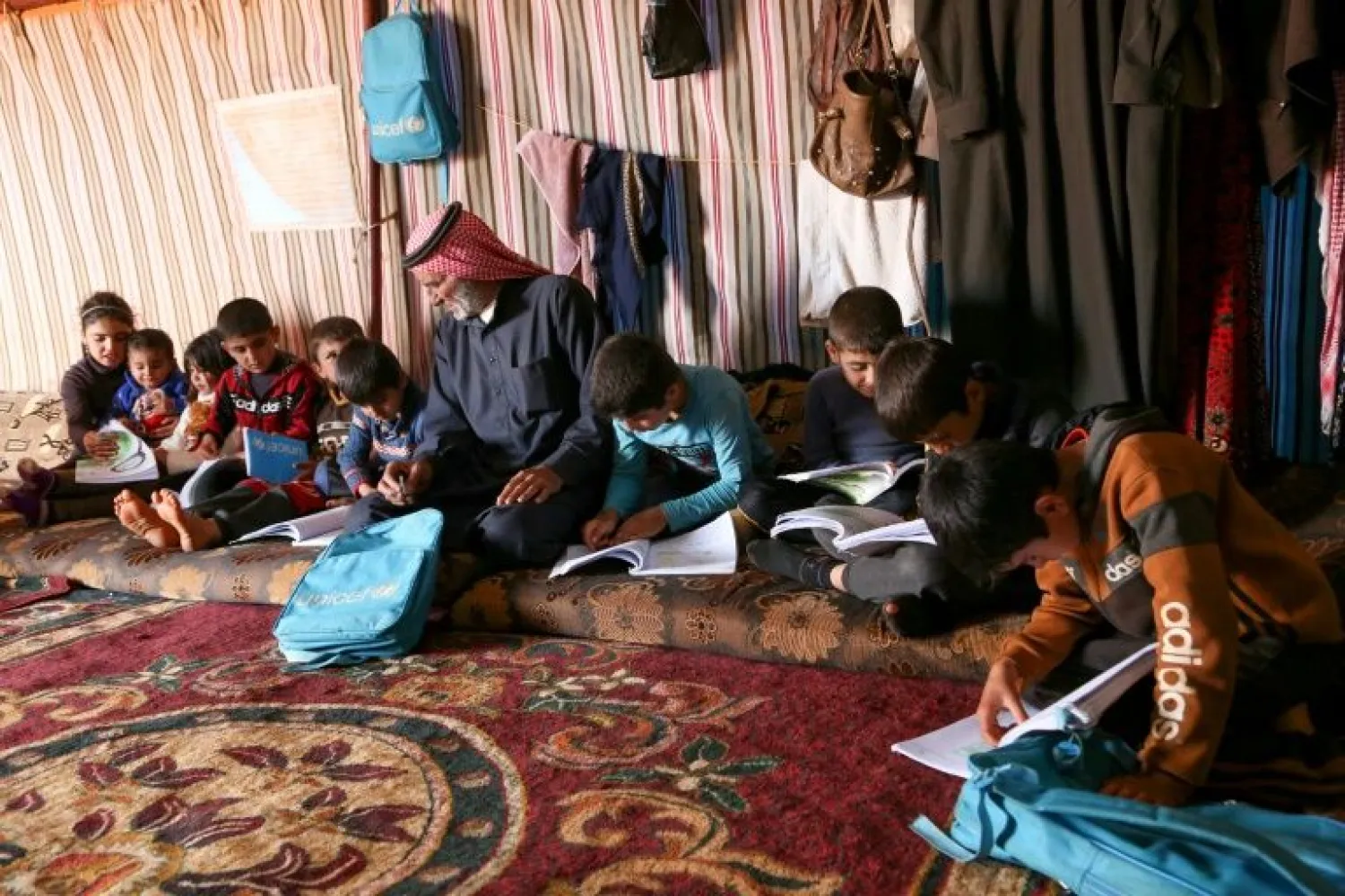 Syrian Abderrazaq Khatoun helps some of his 11 orphaned grandchildren with their school work inside a tent they call come in an encampment in the northwestern Syrian province of Idlib - AFP