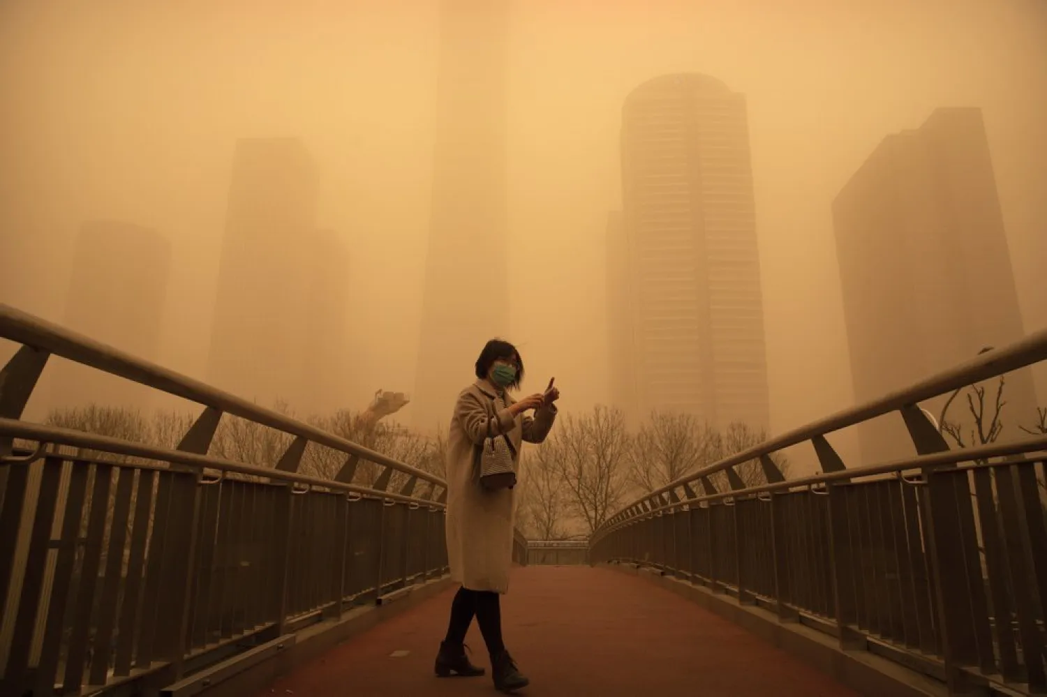 A woman walks along a pedestrian bridge amid a sandstorm during the morning rush hour in the central business district in Beijing, Monday, March 15, 2021. (AP)