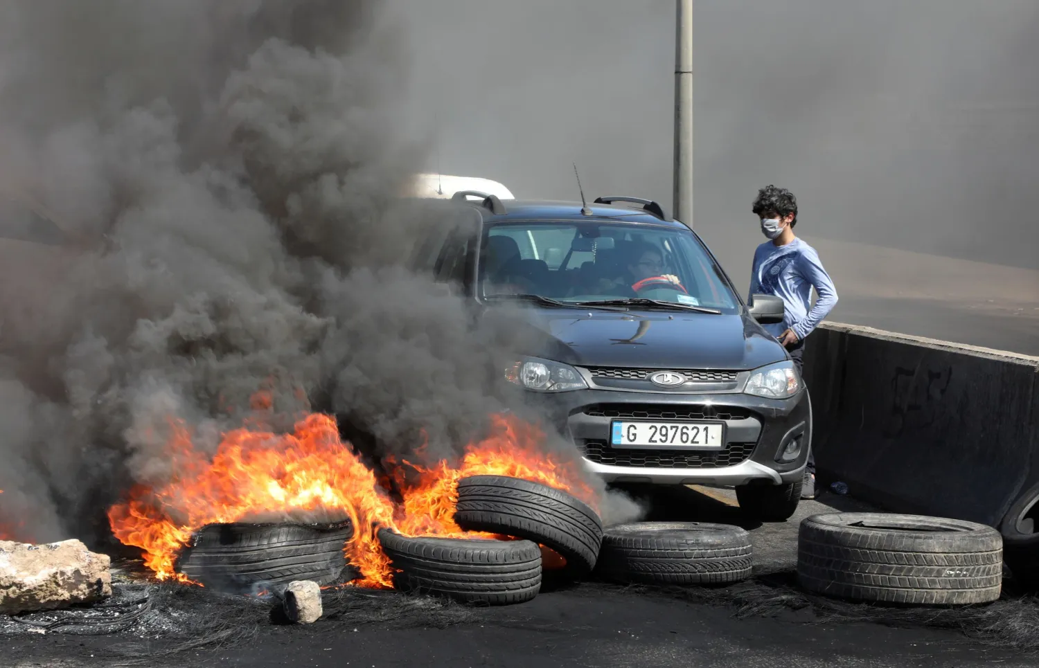 A woman tries to cross a blocked road with burning tires during a protest against the fall in Lebanese pound currency and mounting economic hardships in Khaldeh, Lebanon March 8, 2021. Reuters